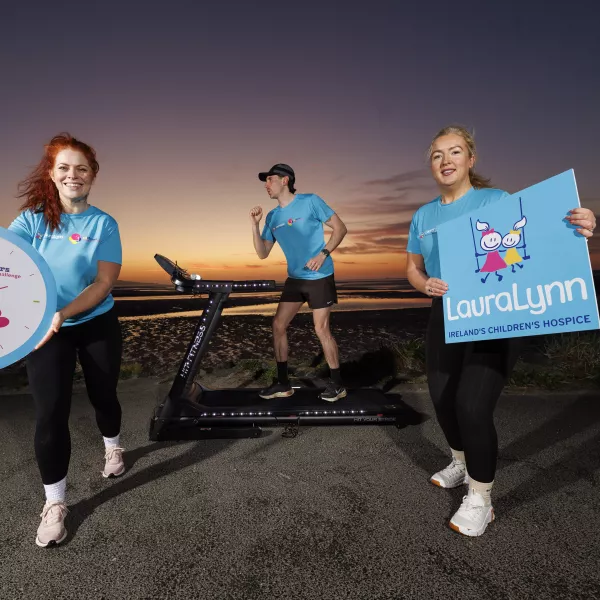 Sunrise at Sandymount Strand. There is a person running on a treadmill. Two other people are holding boards that say 24 hour treadmill challenege and LauraLynn. 