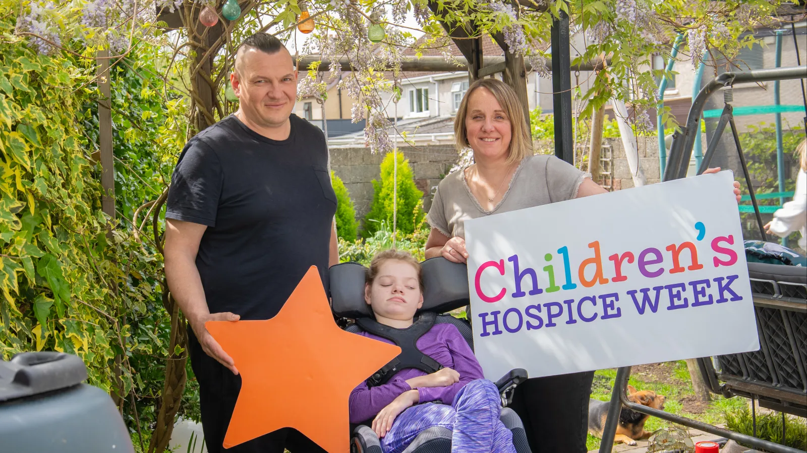 Malgosia's parents standing with Malgosia holdin Children's Hospice Week Branding